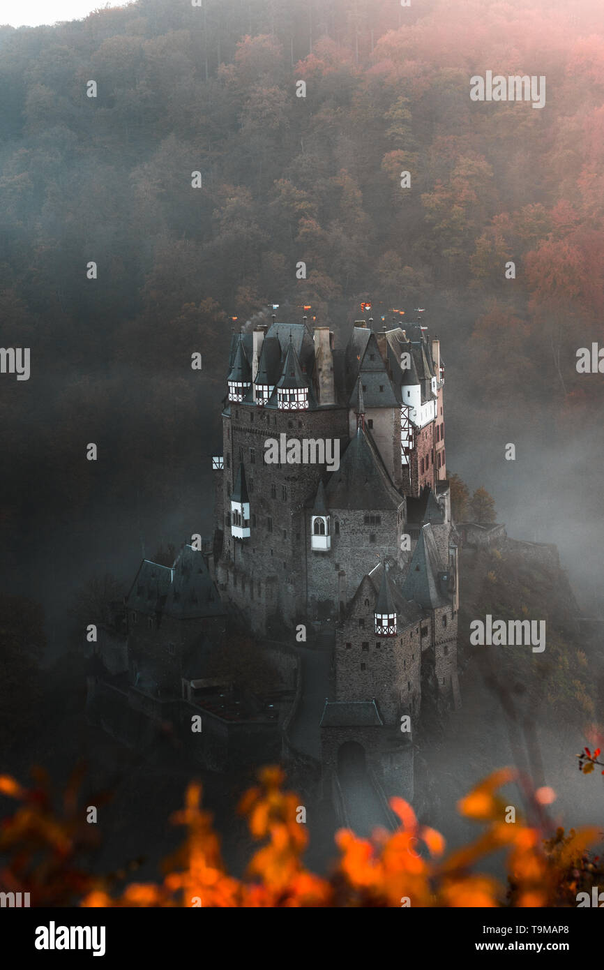 / Burg Eltz Château Eltz pendant le coucher du soleil sur un jour d'automne brumeux d'orangers et de feuilles et le brouillard roulant à travers la vallée (Wierschem, Allemagne) Banque D'Images