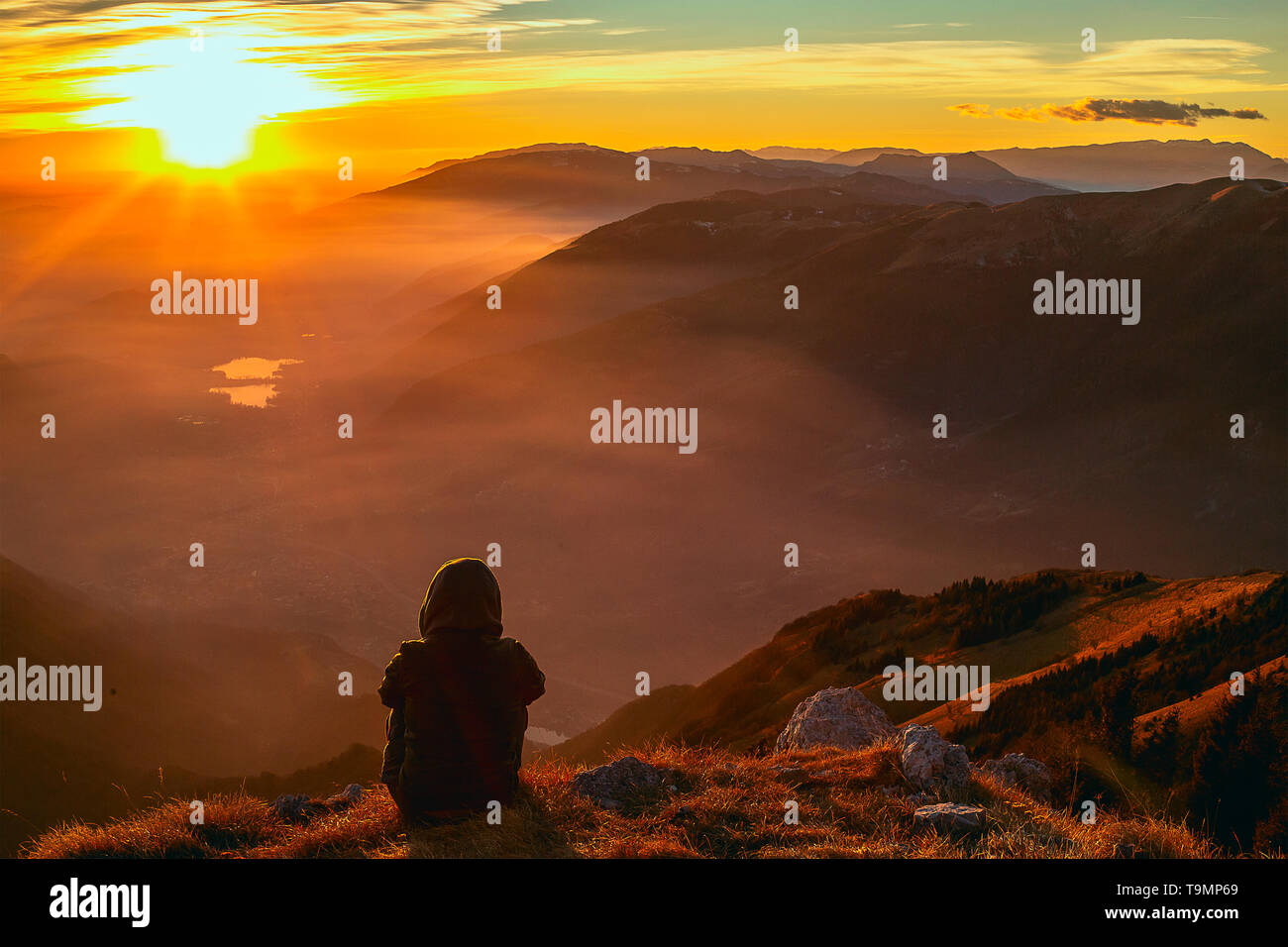 Moment de solitude sur le sommet rocheux exposés. L'homme en noir profitez d'une vue merveilleuse. S'asseoir sur le pic de roche et de regarder dans le quartier coloré de la brume et le brouillard en fo Banque D'Images