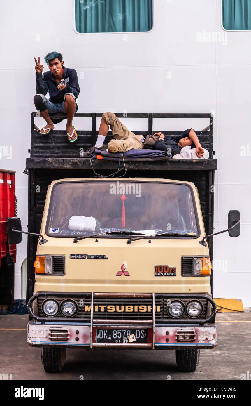 Bali, Indonésie - 25 Février 2019 : deux jeune homme en attente sur le dessus de leur camion stationné. L'un dort, l'autre montre V-sign. Banque D'Images