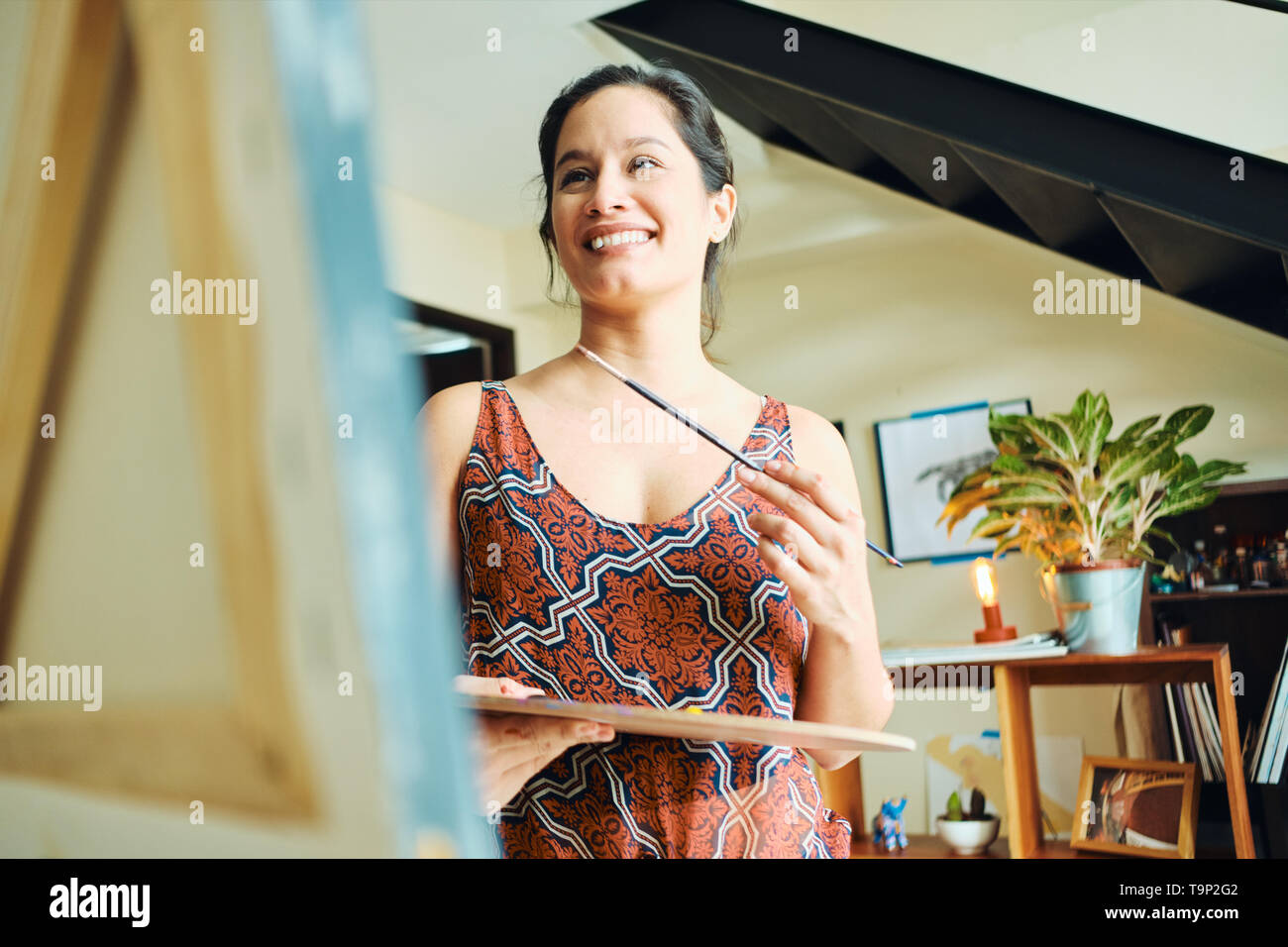 Portrait of Hispanic woman painting dans son home studio, l'exercice de peinture, pinceau, chevalet et couleur pour passe-temps. Banque D'Images