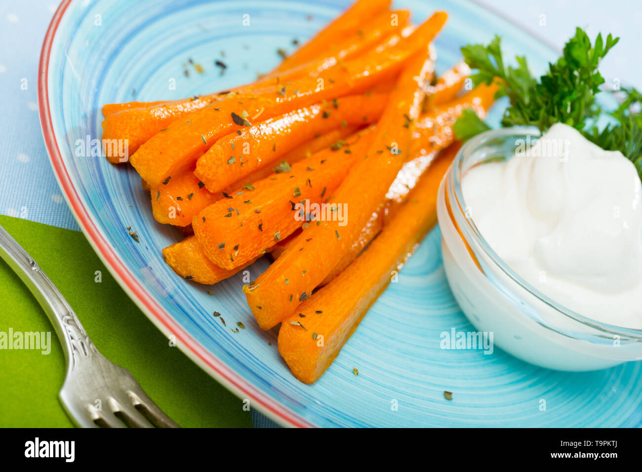 Vitrage savoureux bâtonnets de carottes sur plaque bleue avec de la sauce crème et vert frais Banque D'Images