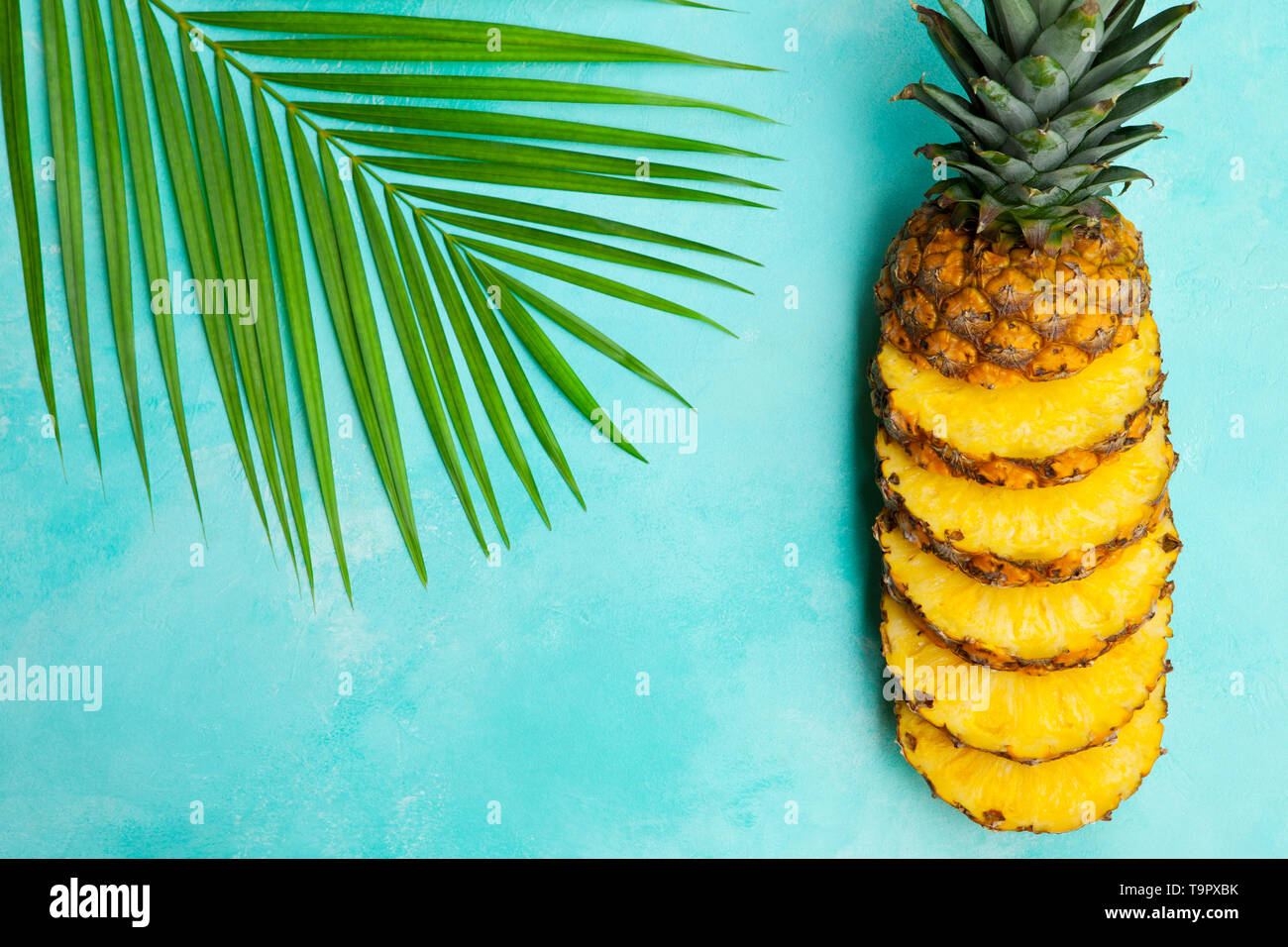 Les tranches d'ananas frais avec des feuilles de palmiers sur fond bleu. Vue d'en haut. Copier l'espace. Banque D'Images