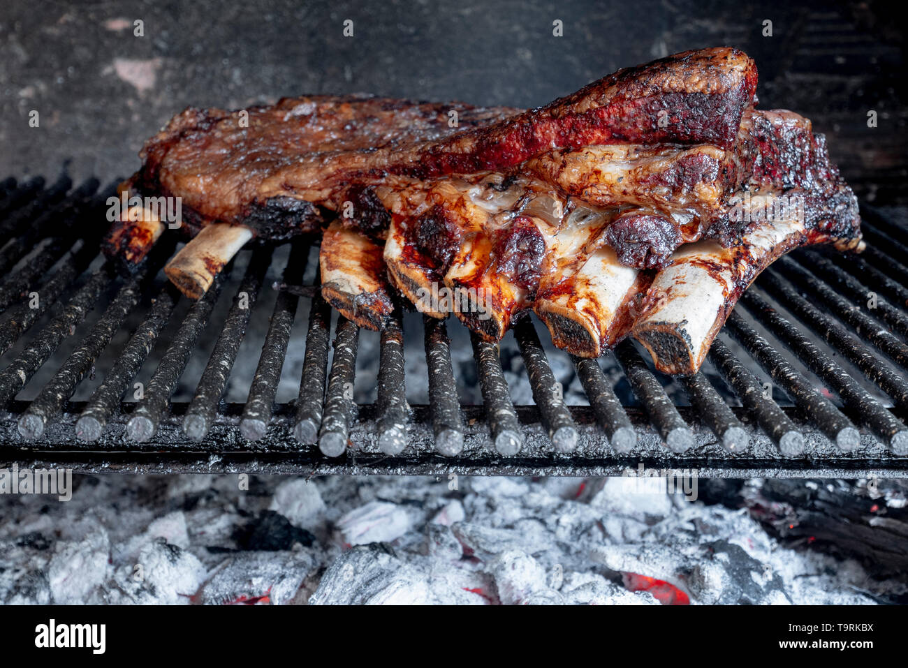 Rôti, viande avec une nervure Argentin typique cuit sur le gril pendant plusieurs heures sur un feu direct avec le charbon de bois et bois de chauffage. Banque D'Images