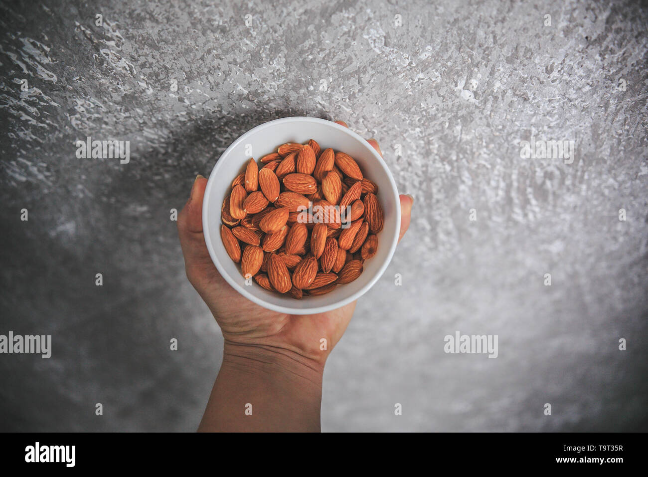 Les amandes avec la peau sans coquille dans le bol blanc tenant dans la main sur le fond blanc et gris. Banque D'Images