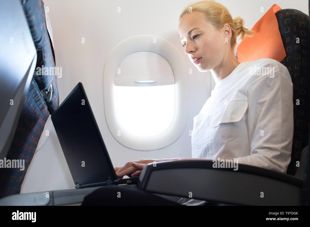 Jolie femme caucasienne travaillant au passager ordinateur portable moderne en utilisant la connexion sans fil à bord du vol de l'avion commercial Banque D'Images