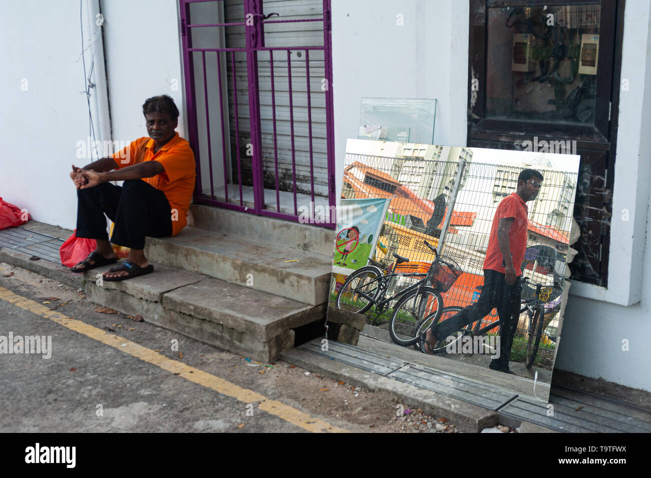10.05.2019, Singapour, République de Singapour, en Asie - Un homme est assis au bord de la route dans la région de Little India comme un passant se reflète dans un miroir. Banque D'Images