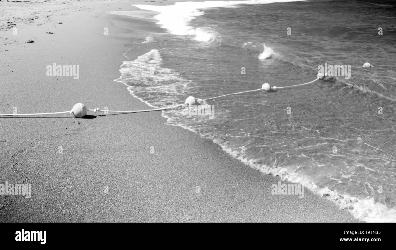 Image en noir et blanc de la bouée de sauvetage sur la ligne de corde posée sur la mer et plage de sable sur la surface de l'eau flotaing Banque D'Images