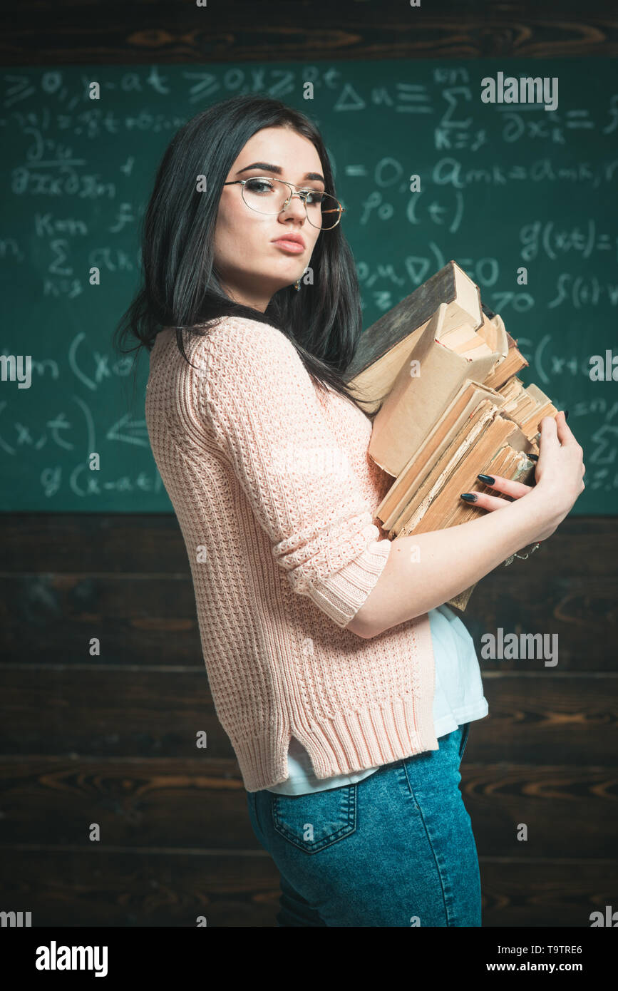 Vue latérale brunette étudiante avec deux tas de livres. Smart college girl en portant des lunettes cardigan rose va à la bibliothèque Banque D'Images