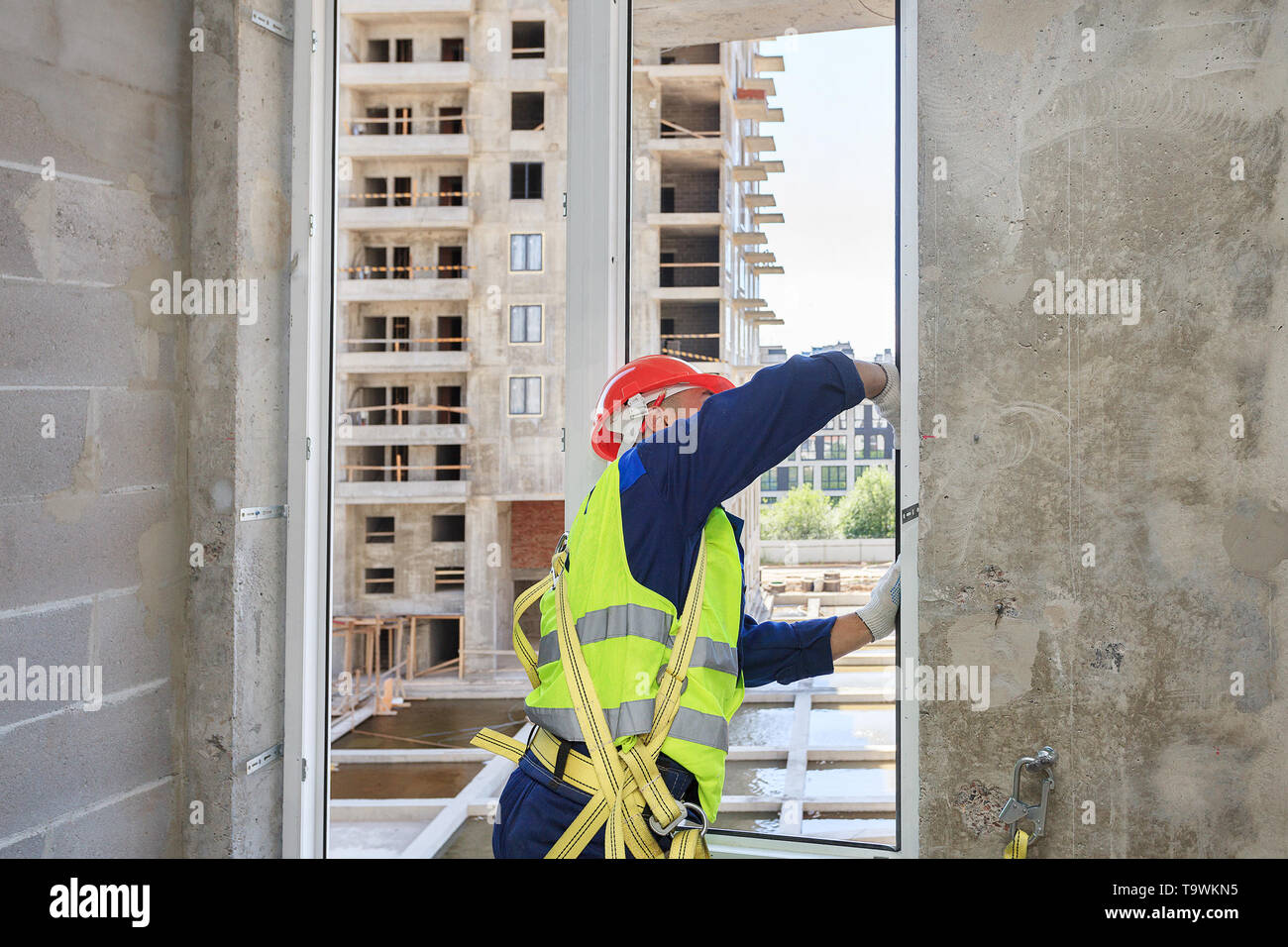 Un travailleur dans un casque orange installe un double-vitrage dans une nouvelle maison, dans un contexte de construction. Banque D'Images