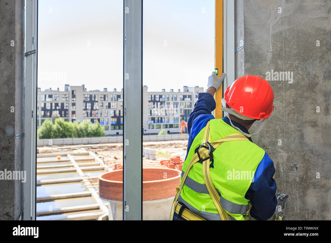 Un travailleur dans un casque orange installe un double-vitrage dans une nouvelle maison, dans un contexte de construction. Banque D'Images