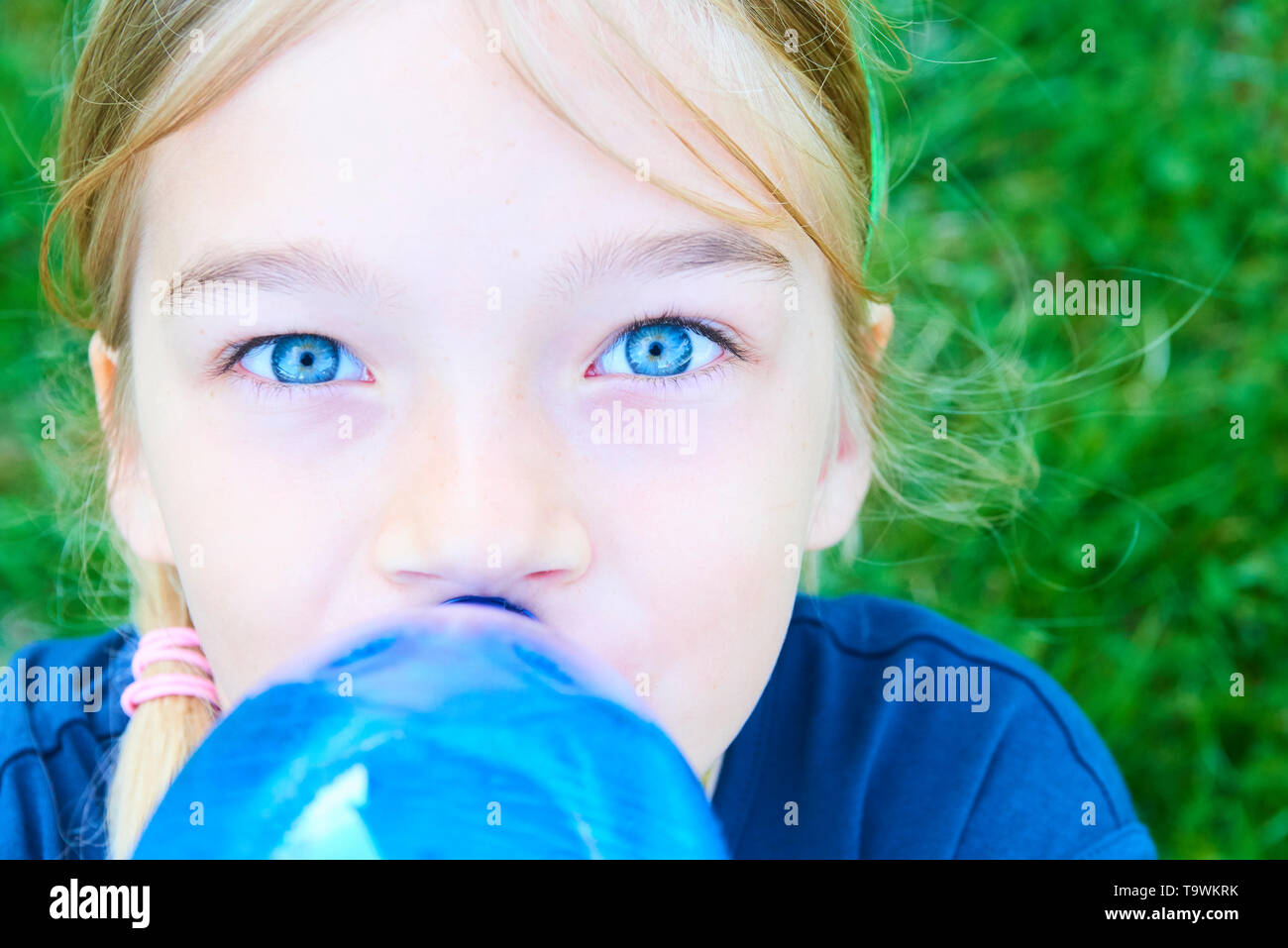 Close up portrait of girl adorable aux yeux bleus l'eau potable de la bouteille bleue en plastique avec fond de verdure Banque D'Images