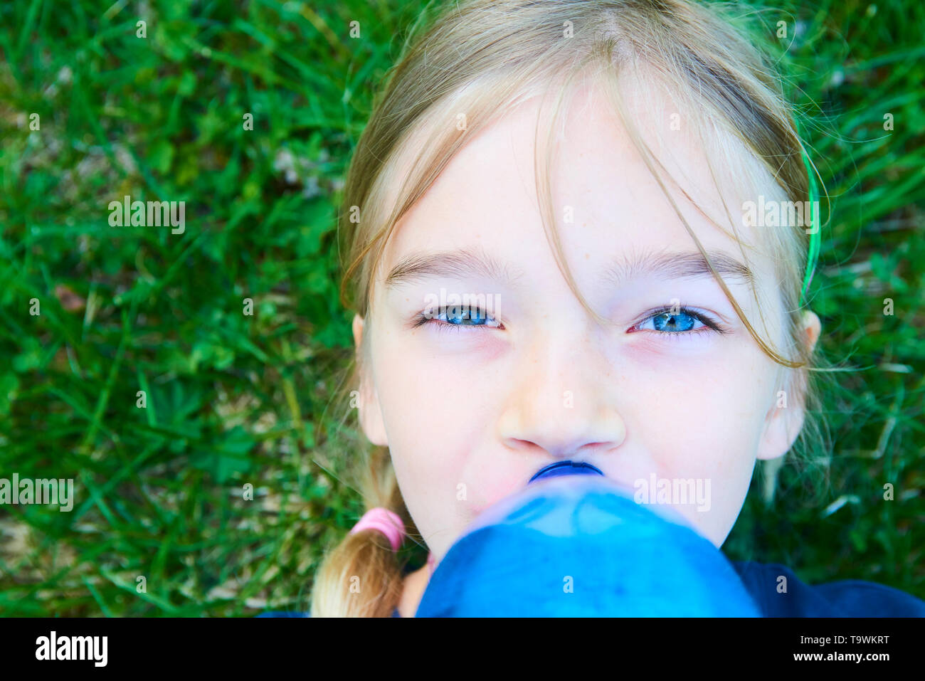 Close up portrait of girl adorable aux yeux bleus l'eau potable de la bouteille bleue en plastique avec fond de verdure Banque D'Images
