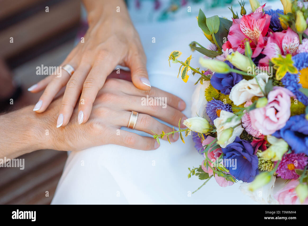 Mains avec des anneaux sur les doigts de la mariée et marié sur le fond d'un bouquet de mariage Banque D'Images