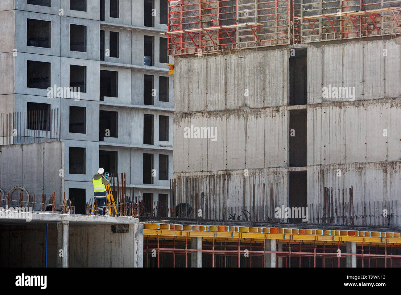 Le constructeur en salopette jaune fait une étude topographique dans le contexte d'un mur en béton, un immeuble en construction. Banque D'Images