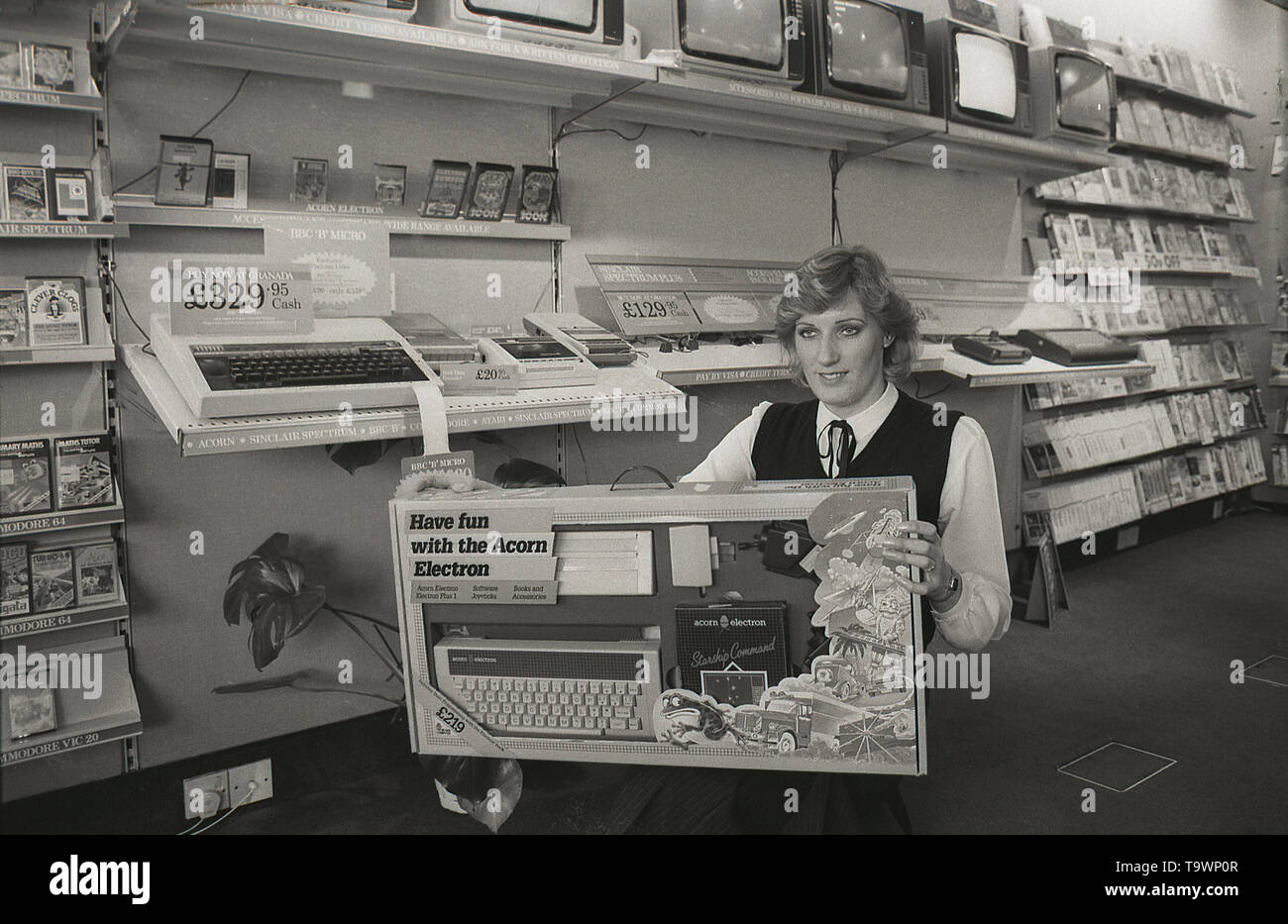 1985, historique, équipement home cinéma à l'intérieur d'un magasin de détail Granada TV, une femelle shop assistant affiche une boîte contenant la nouvelle Acorn Electron accueil ordinateur, England, UK. Banque D'Images