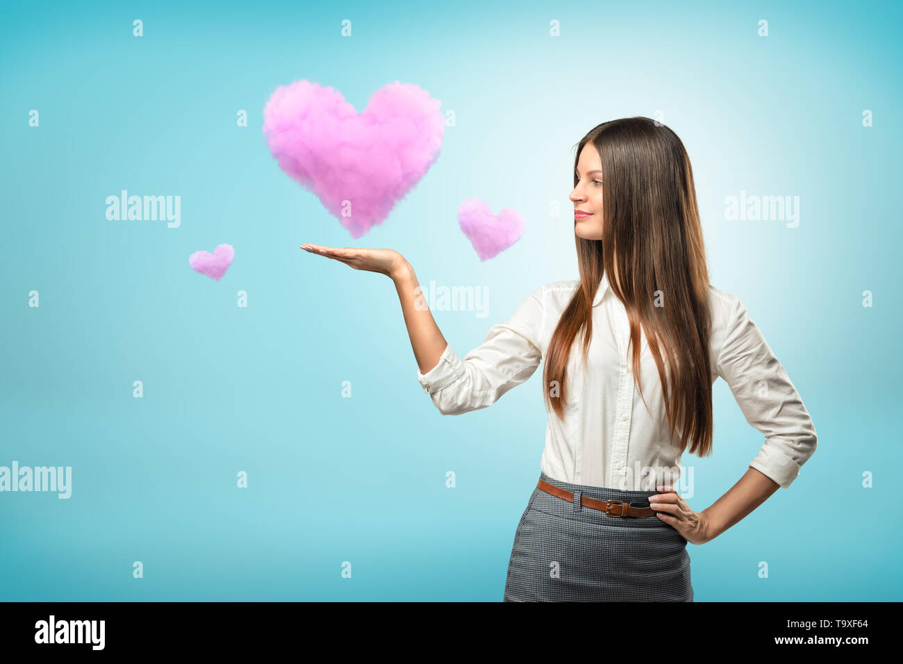 Young businesswoman holding nuage rose coeur sur sa main sur fond bleu Banque D'Images