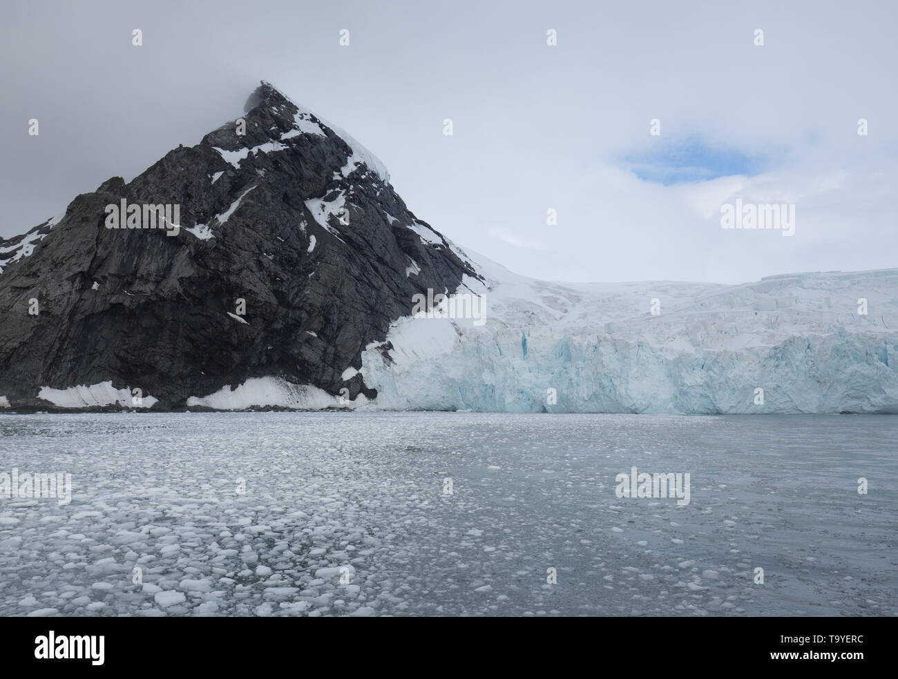 Une falaise de pierre gris foncé émergeant de l'océan Atlantique avec un glacier tomber à l'eau, dans l'Antarctique. Banque D'Images