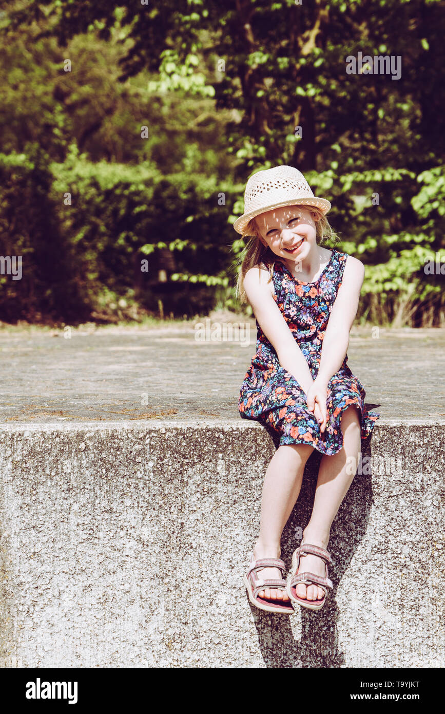 Portrait of cute smiling girl wearing hat assis sur mur de retenue Banque D'Images
