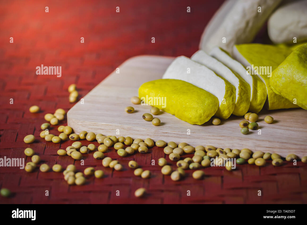 Le Tofu est coupé en tranches sur une planche à découper en bois et graines de soja éparpillés sur la table. Concept d'aliments sains. Banque D'Images