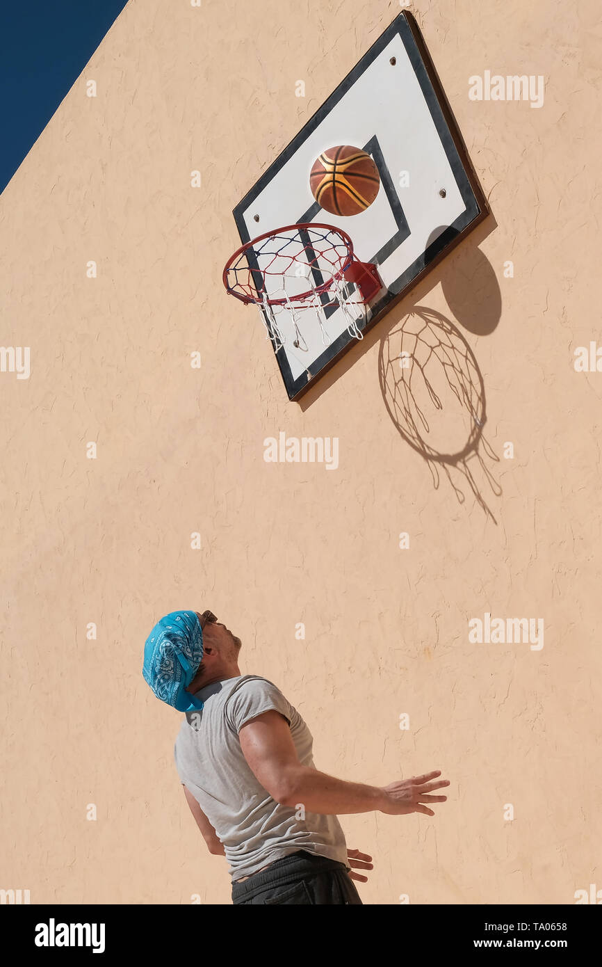 Un homme jouant au basket-ball. La balle et le filet de créer des ombres sur le mur jaune. Banque D'Images