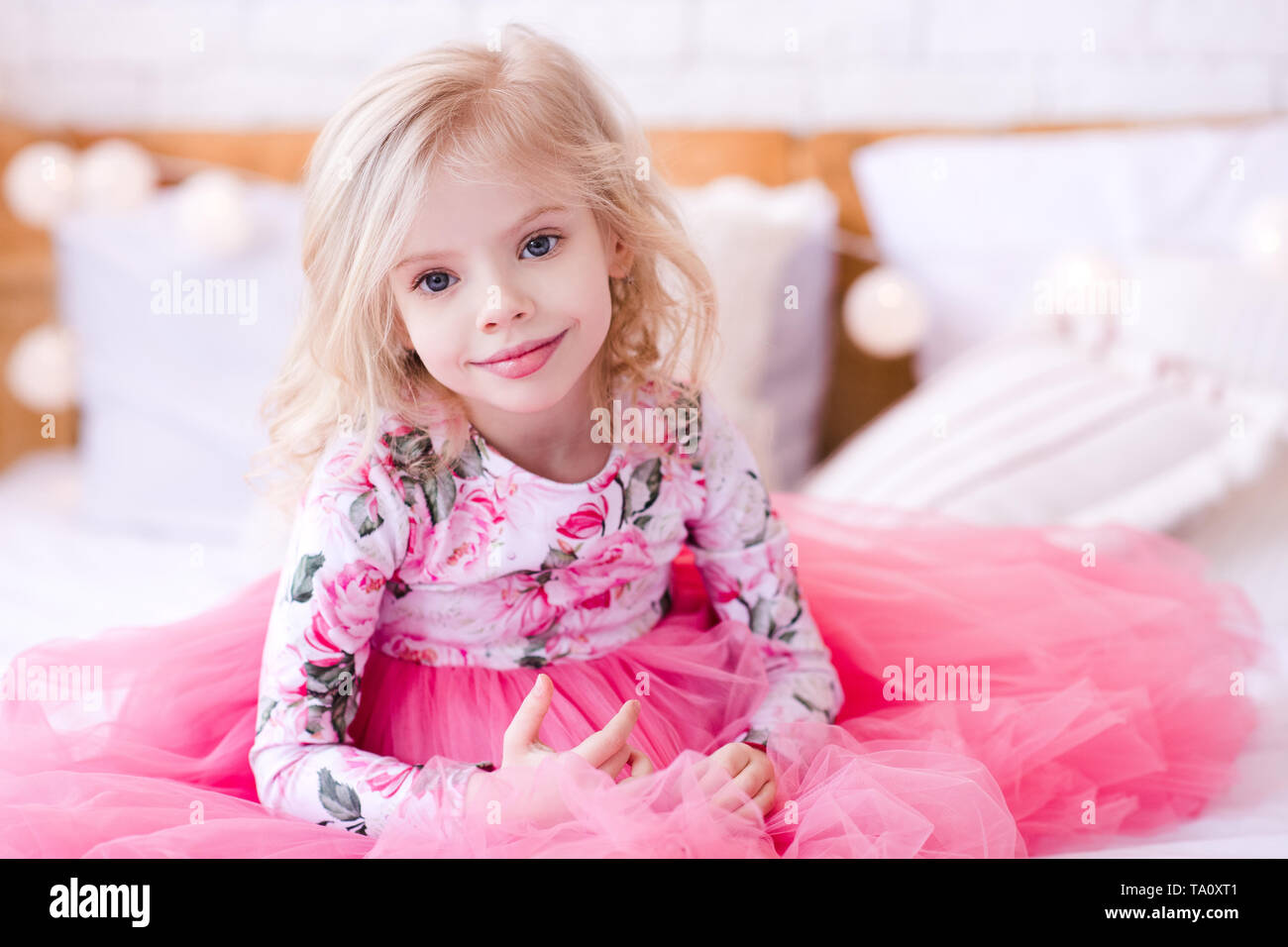 Smiling baby girl princess 3-4 ans portant robe rose élégant assis au lit libre. En regardant la caméra. L'enfance. Banque D'Images