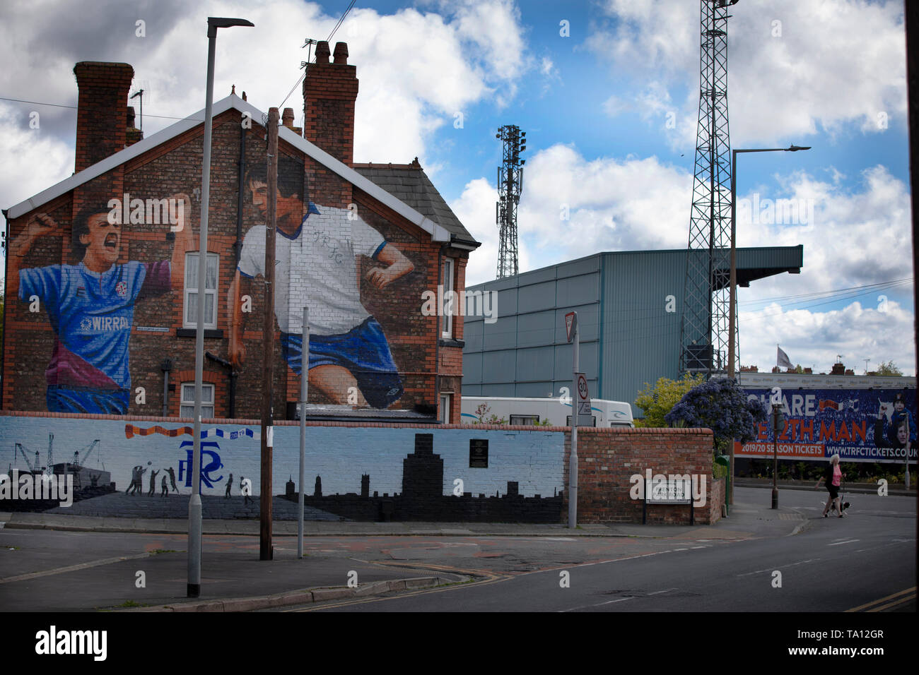 Une femme marche un chien passé une peinture murale de l'artiste Paul Curtis sur un pignon de la fin d'une maison à Wirral Prenton, représentant deux joueurs de Tranmere Rovers. La murale est situé juste à l'extérieur du stade du club, Prenton Park. Tranmere Rovers acquise à la promotion de la Ligue 2 à partir de l'EFL Ligue nationale via un play-off dans la saison 2017-8 et est retourné à Wembley 12 mois plus tard le 25 mai pour faire face à Newport County pour une place dans une ligue étrangère. Banque D'Images
