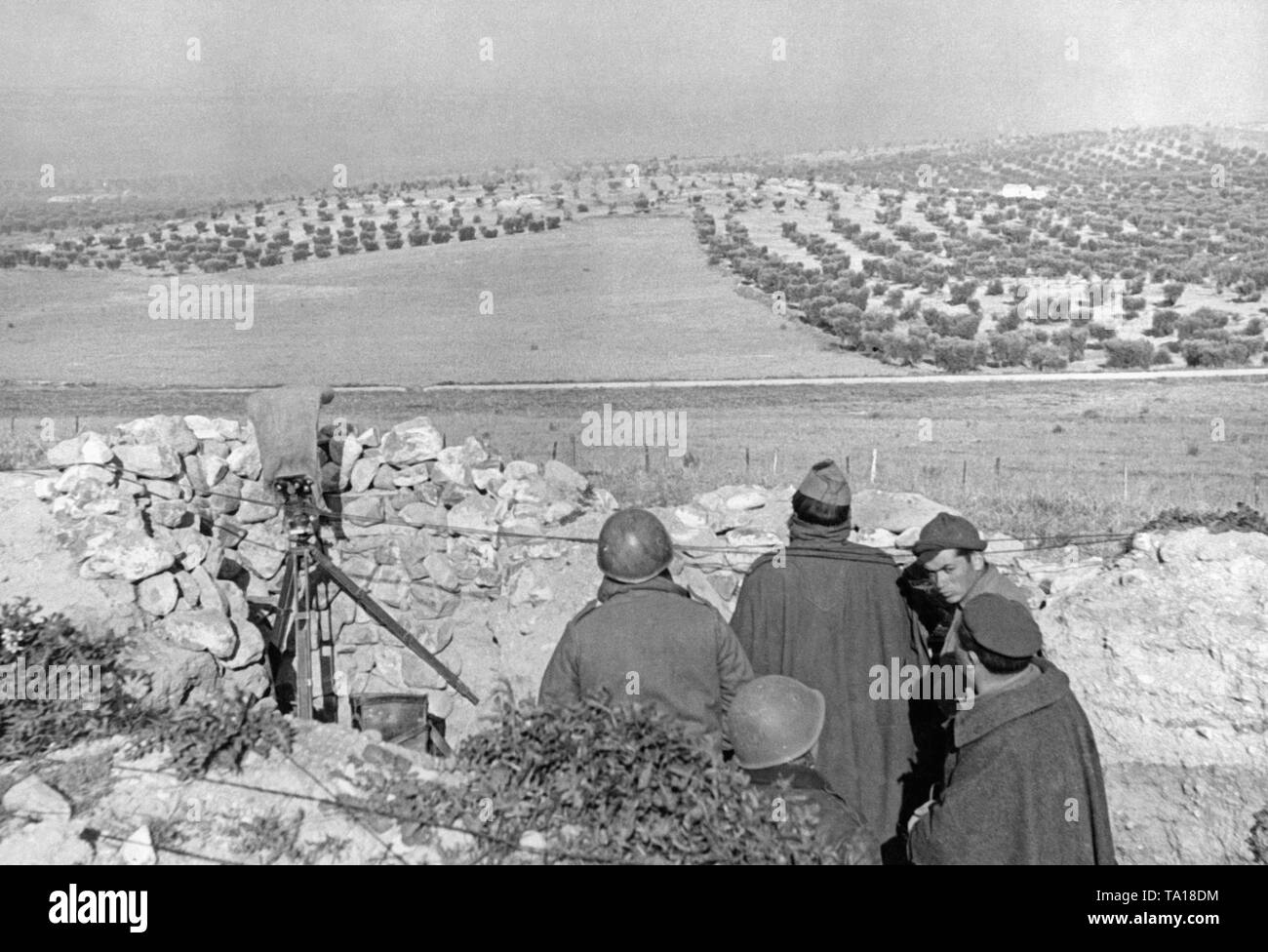 Photo de légionnaires italiens (en manteau avec un chapeau ou casque d'acier) dans une position d'observation à l'avant dans la guerre civile espagnole. Sur la gauche, un télescope de ciseaux. Dans l'arrière-plan, une plantation d'oliviers. Banque D'Images