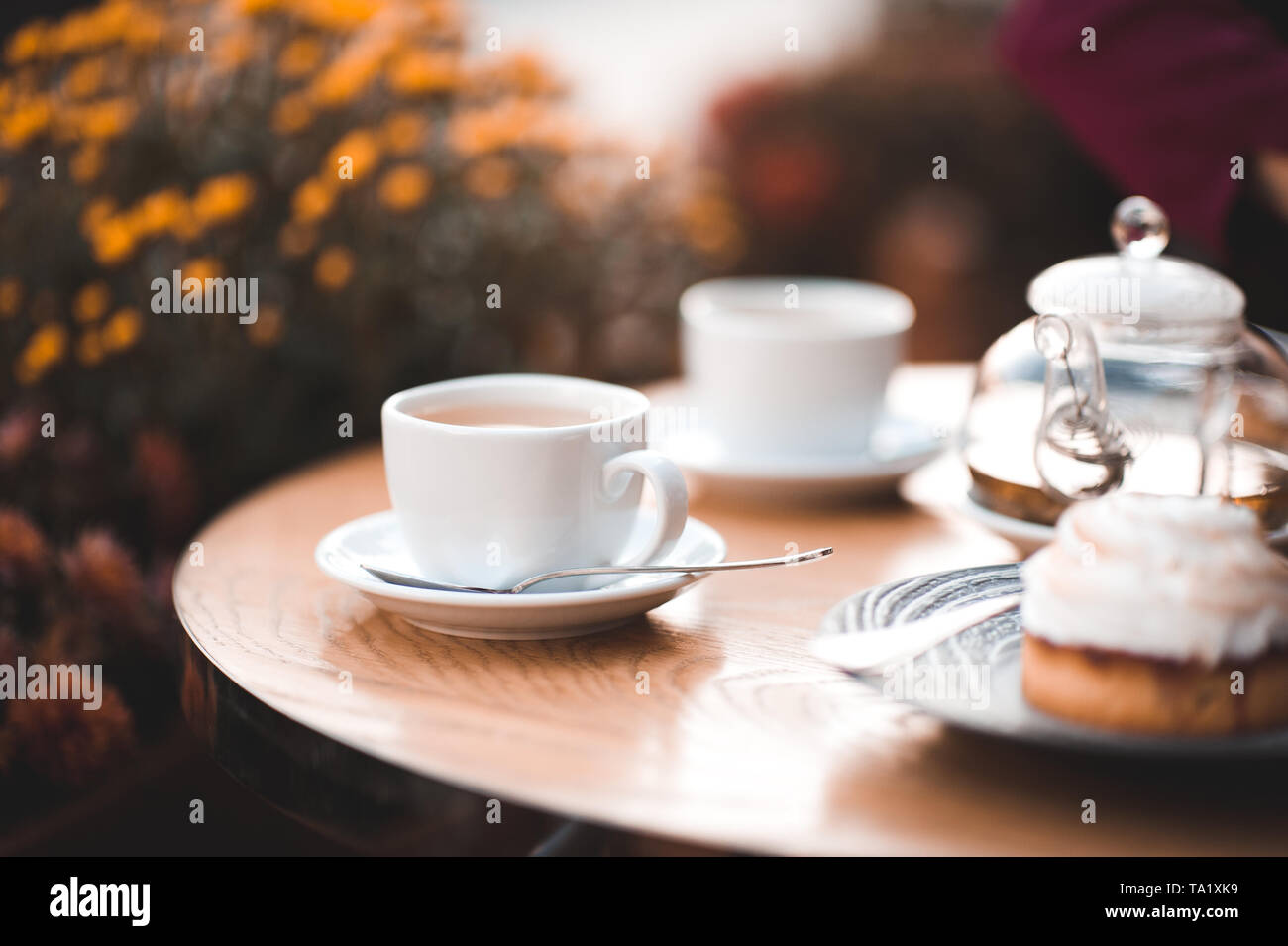 Tasse de thé avec du gâteau sur la table en bois dans le café avec des fleurs à l'arrière-plan. Bonjour. Banque D'Images