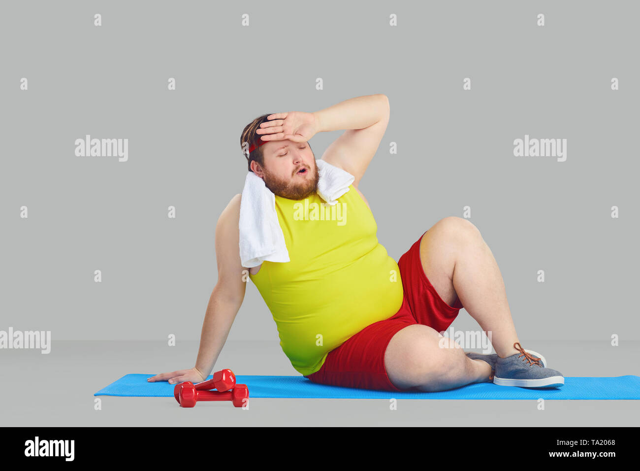 Un gros homme dans les vêtements de sport fatigué essuie le sueur de son  front assis sur le plancher sur un arrière-plan gris Photo Stock - Alamy