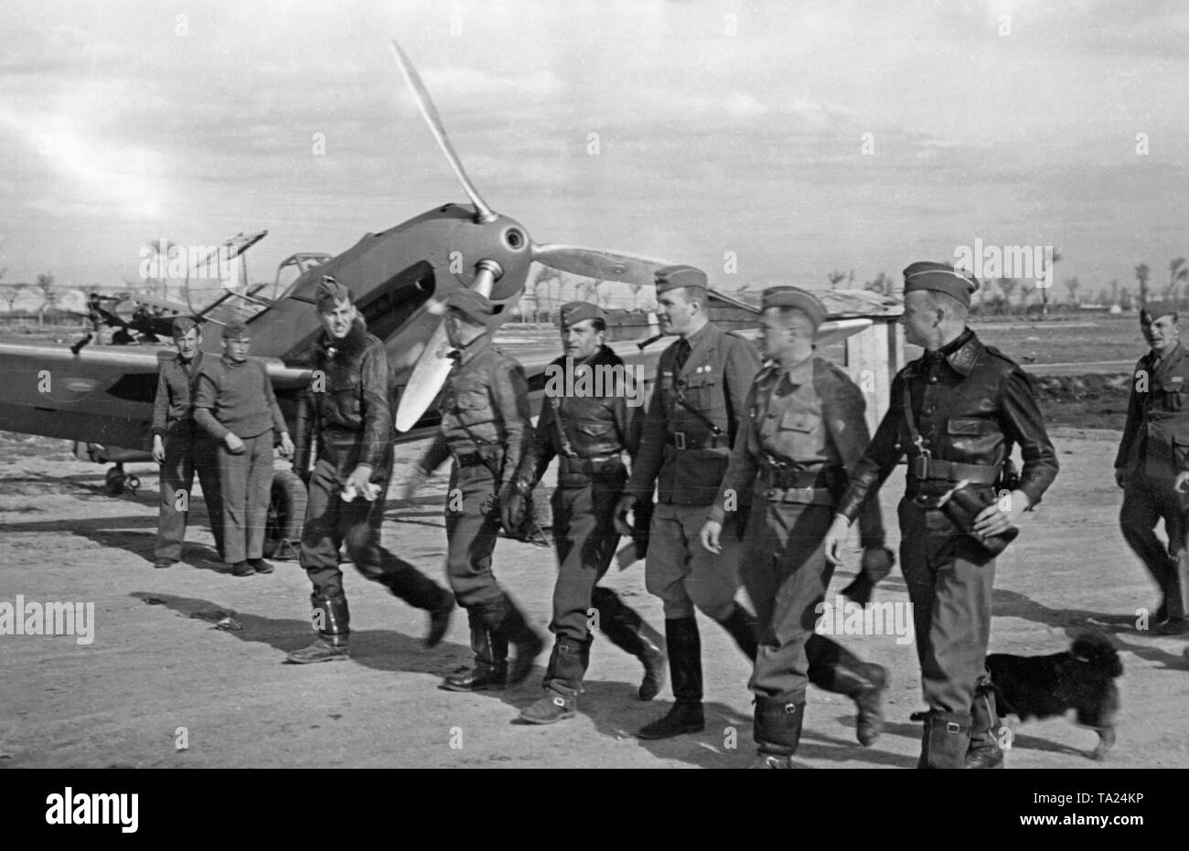 Photo d'un groupe de pilotes de combat de la légion Condor, groupe de combat 88, en marchant à leur prêt-à-utiliser Messerschmitt Bf 109 combattants (à l'arrière-plan) sur un aérodrome en Espagne en 1939. La bouche de la mitrailleuse est visible dans le creux de l'hélice et le cône de. Banque D'Images