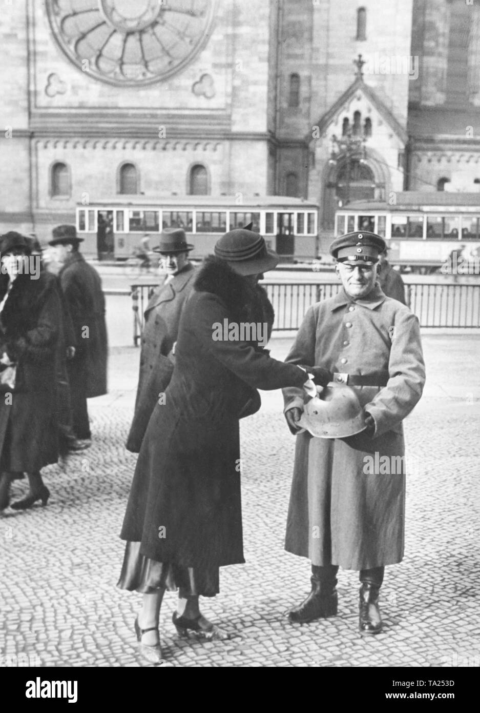 Un membre en uniforme avec un appariement Stahlhelm casque et conteneur de ramassage collecte les dons des passants en face de l'Église du Souvenir Kaiser Wilhelm à l'angle de la Tauentzienstrasse et Rankestrasse. Banque D'Images