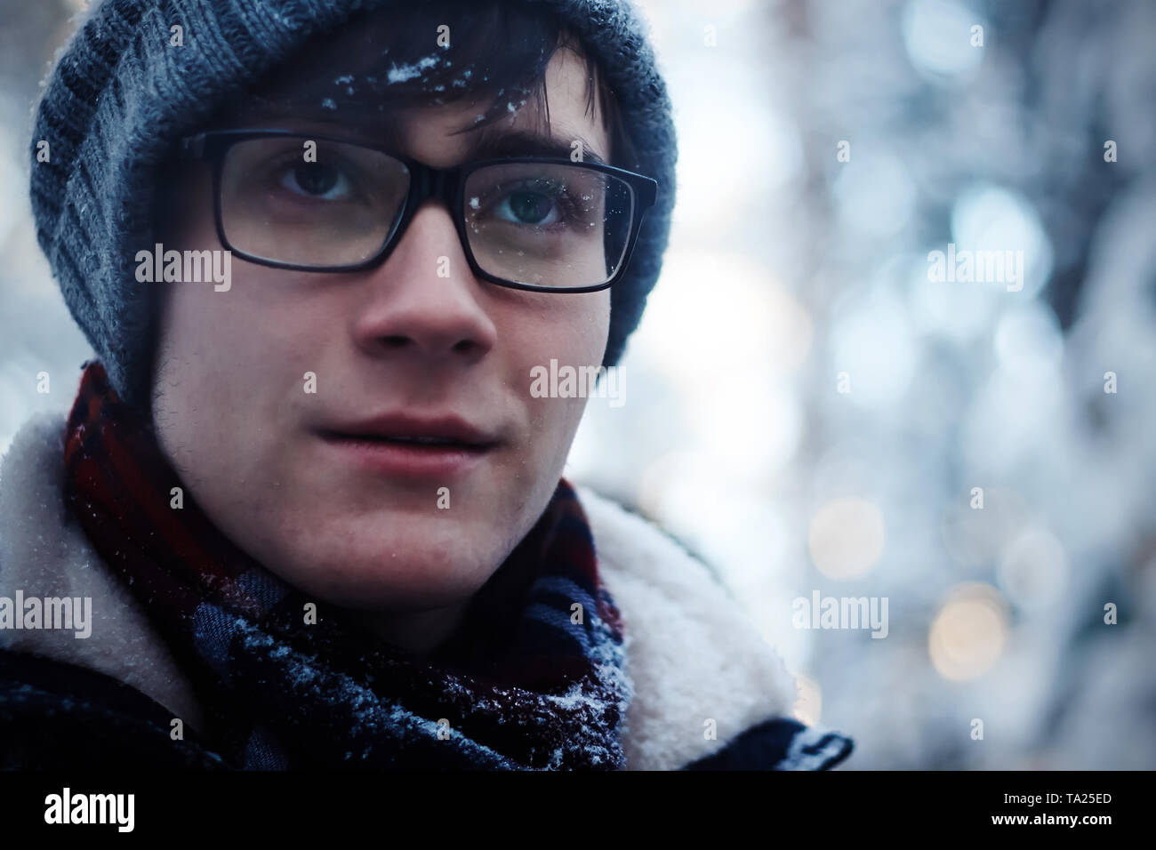 Le mec avec des lunettes et des vêtements d'hiver gèle dans la saison froide. Écharpe, chapeau et lunettes en flocons Banque D'Images