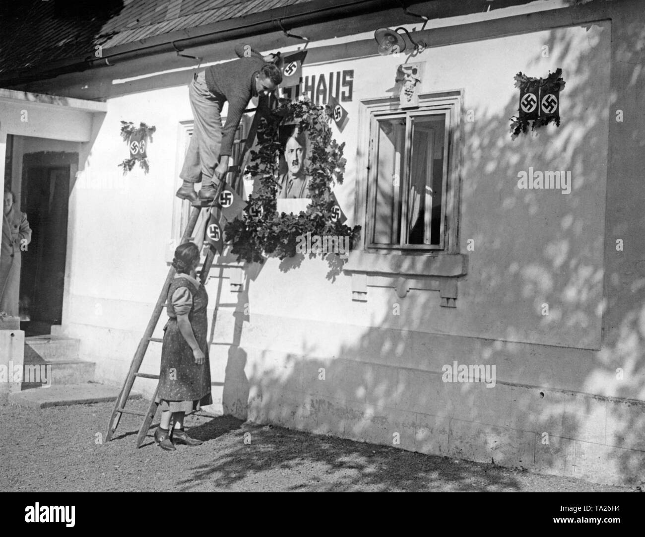 Les résidents d'une maison à Sluknov fixer swastika drapeaux et feuilles de chêne autour d'un portrait de Hitler sur l'housewall le 30 septembre 1938. Banque D'Images