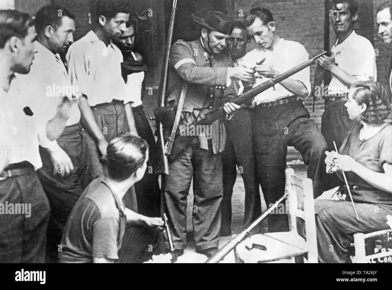 Un membre (au centre) de la Guardia Civil (une unité de police paramilitaire, qui rejoint presque entièrement les troupes de Franco en 1936) forme des milices de la défense civile et d'une femme sur la manipulation d'une carabine. Le policier montre le milicien le verrou retiré de l'arme. Une femme participe également à la formation. Banque D'Images