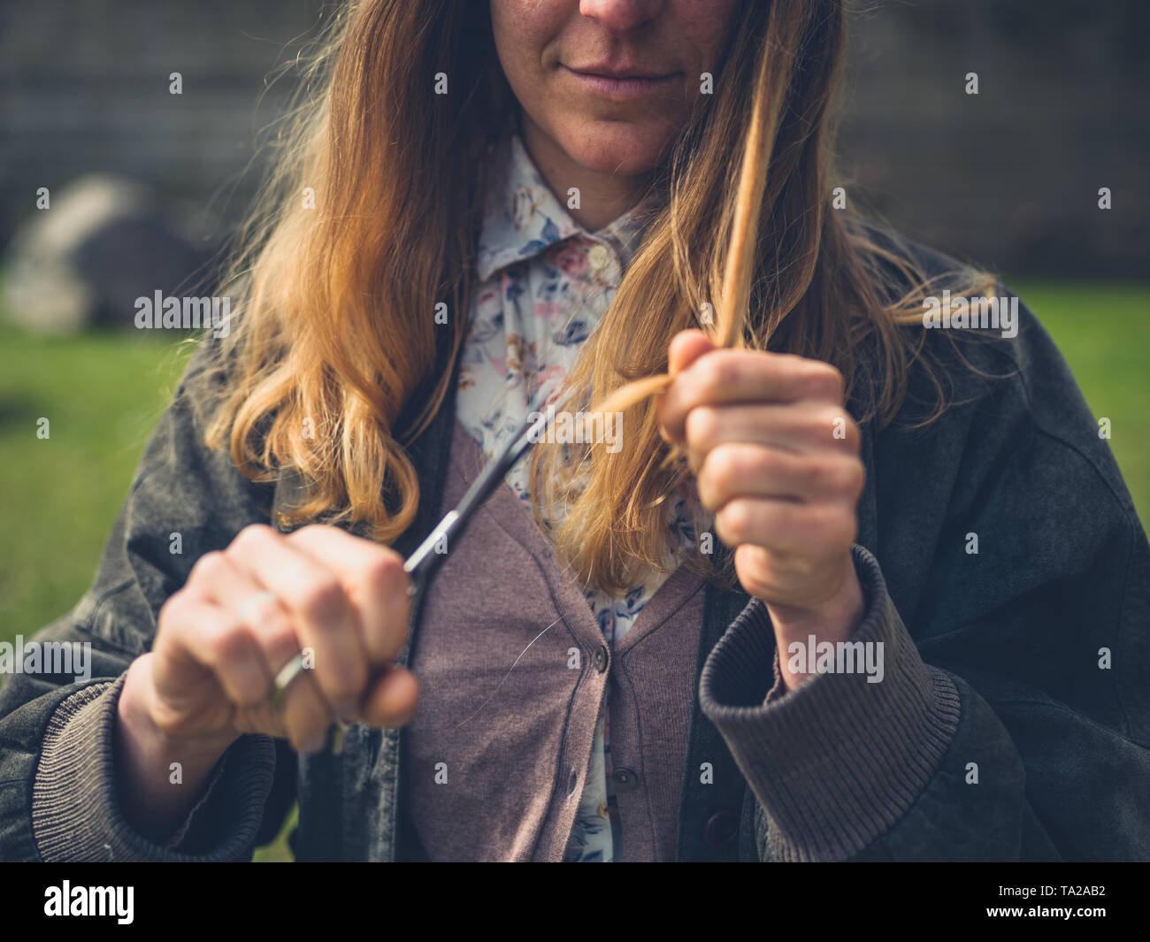 Une jeune femme coupe ses cheveux et les pointes fourchues en plein air Banque D'Images