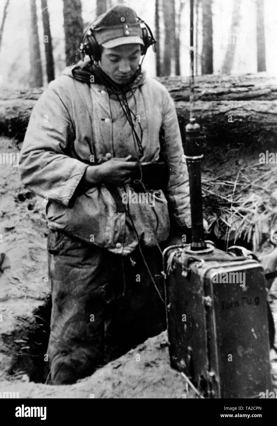 L'opérateur radio à un poste de commandement de l'entreprise l'écoute d'un message. En face de lui sa radio portative. Il porte l'uniforme de camouflage d'hiver matelassé. Photo de l'entreprise de propagande (PK) : correspondant de guerre Kuehn. Banque D'Images