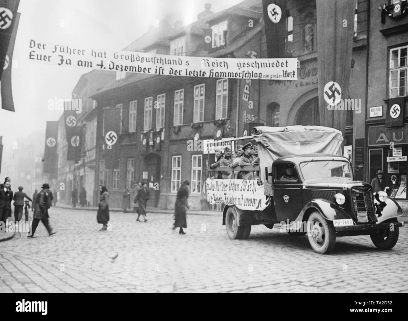 Voiture de l'Ordnungspolizei (police régulières de l'Allemagne nazie) avec porte à Tellnitz Telnice (aujourd'hui). La ville est décorée avec des drapeaux à croix gammée. Les Allemands de Sudeten tenir une élection partielle en ce qui concerne l'annexion des Sudètes au Reich allemand. Sur l'affiche sur la rue : "Le führer a forgé le grand Empire Allemand / Votre Oui le 4 décembre est le dernier coup de marteau sur l'excellent travail". Banque D'Images
