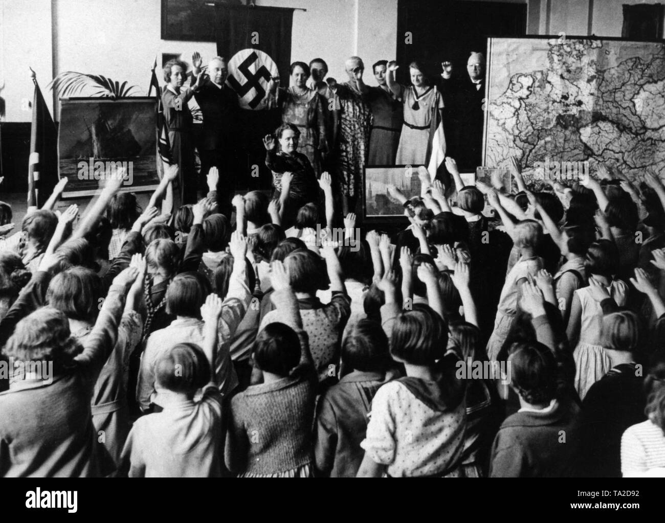 Dans une classe de l'école élémentaire, décoré avec des affiches de propagande de la seconde guerre mondiale, un drapeau à croix gammée et une carte avec les territoires séparés pour le Traité de Versailles, les enseignants et les élèves un honneur national 'celebration' avec le chant de l'hymne national allemand et le Horst Wessel Lied (chant), ainsi que le salut hitlérien. Banque D'Images