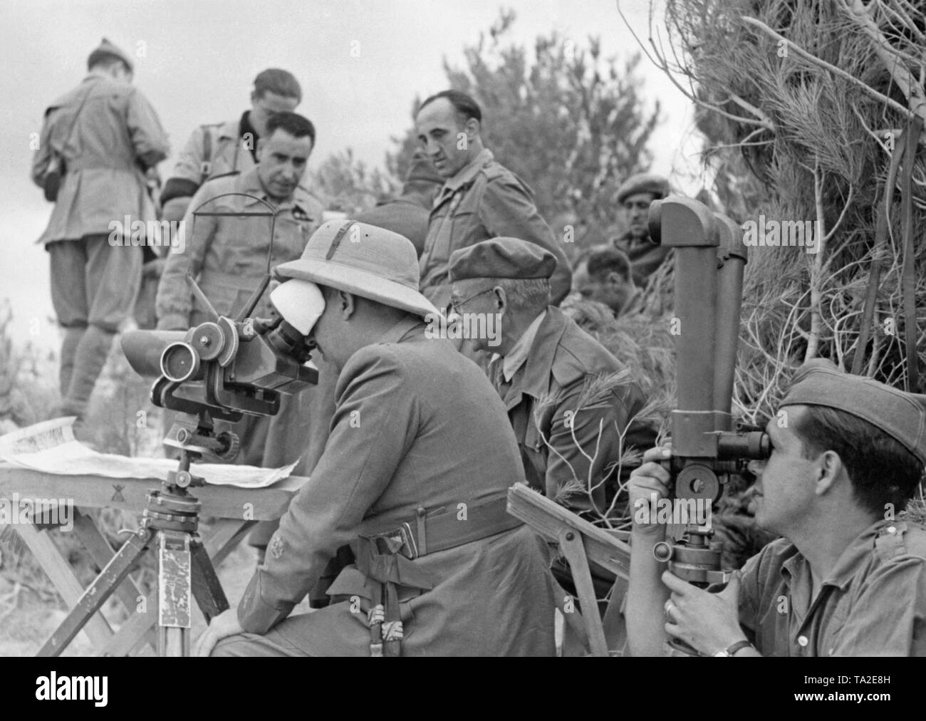 Photo de généralissime Francisco Franco (à l'avant avec un topee, à l'intermédiaire d'un projecteur 35 Flakglas allemand, 10x80) avec le général Emilio Mola Vidal (derrière, avec un béret et sur le terrain au cours de la visite) Tunique d'officiers d'une division de la légion Condor durant la Guerre d'Espagne avant le mois de juin, 1937. Un légionnaire est de regarder à travers un télescope de ciseaux. Derrière les généraux, une table à cartes et des officiers. Banque D'Images