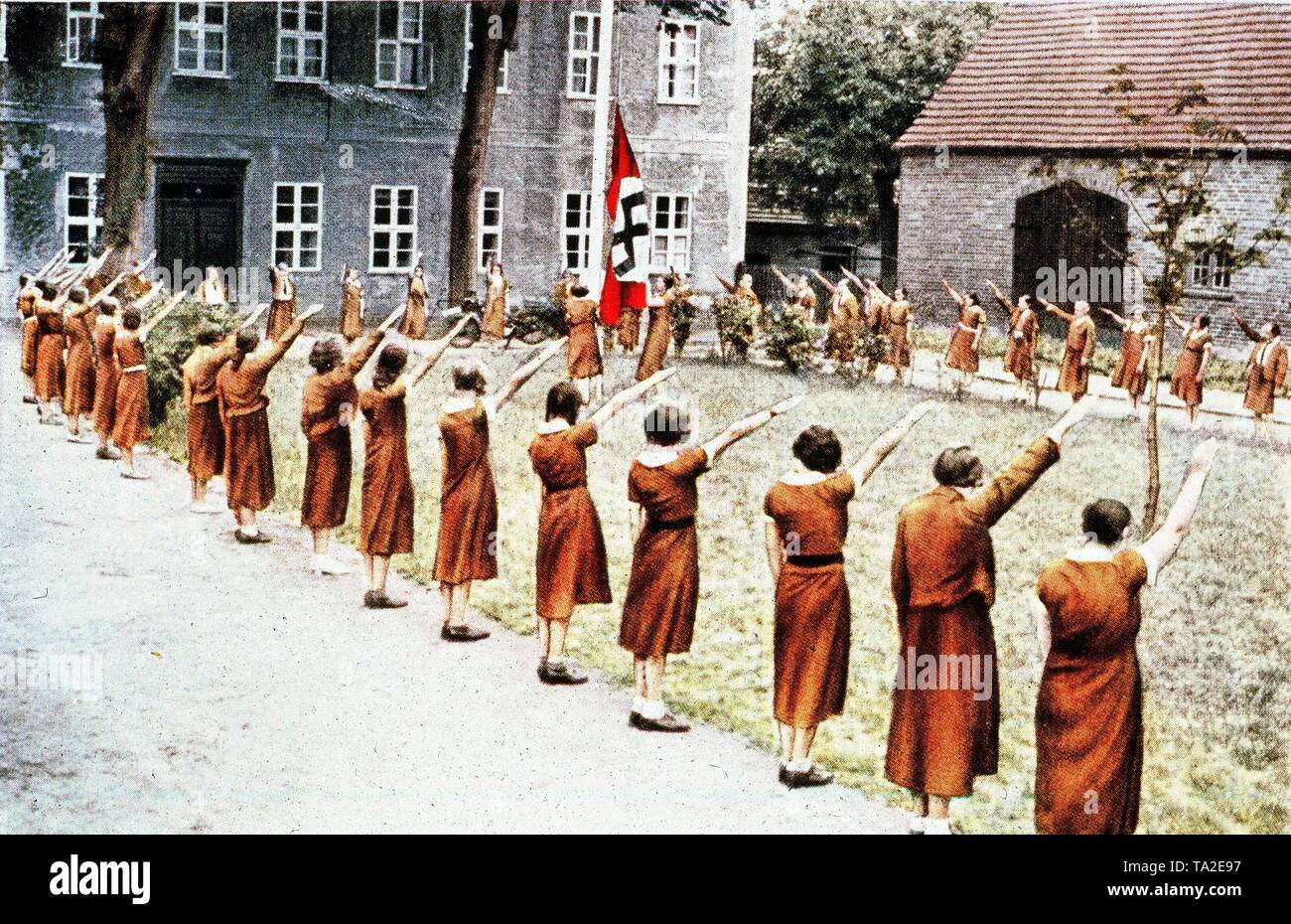 Les filles au cours de la BDM daily morning roll call hissant le drapeau à croix gammée sur le parvis d'un Landjahrheim du NSDAP. En 1939, l'année obligatoire a été introduite pour la plupart des filles allemandes et les femmes de moins de 25 ans. Banque D'Images