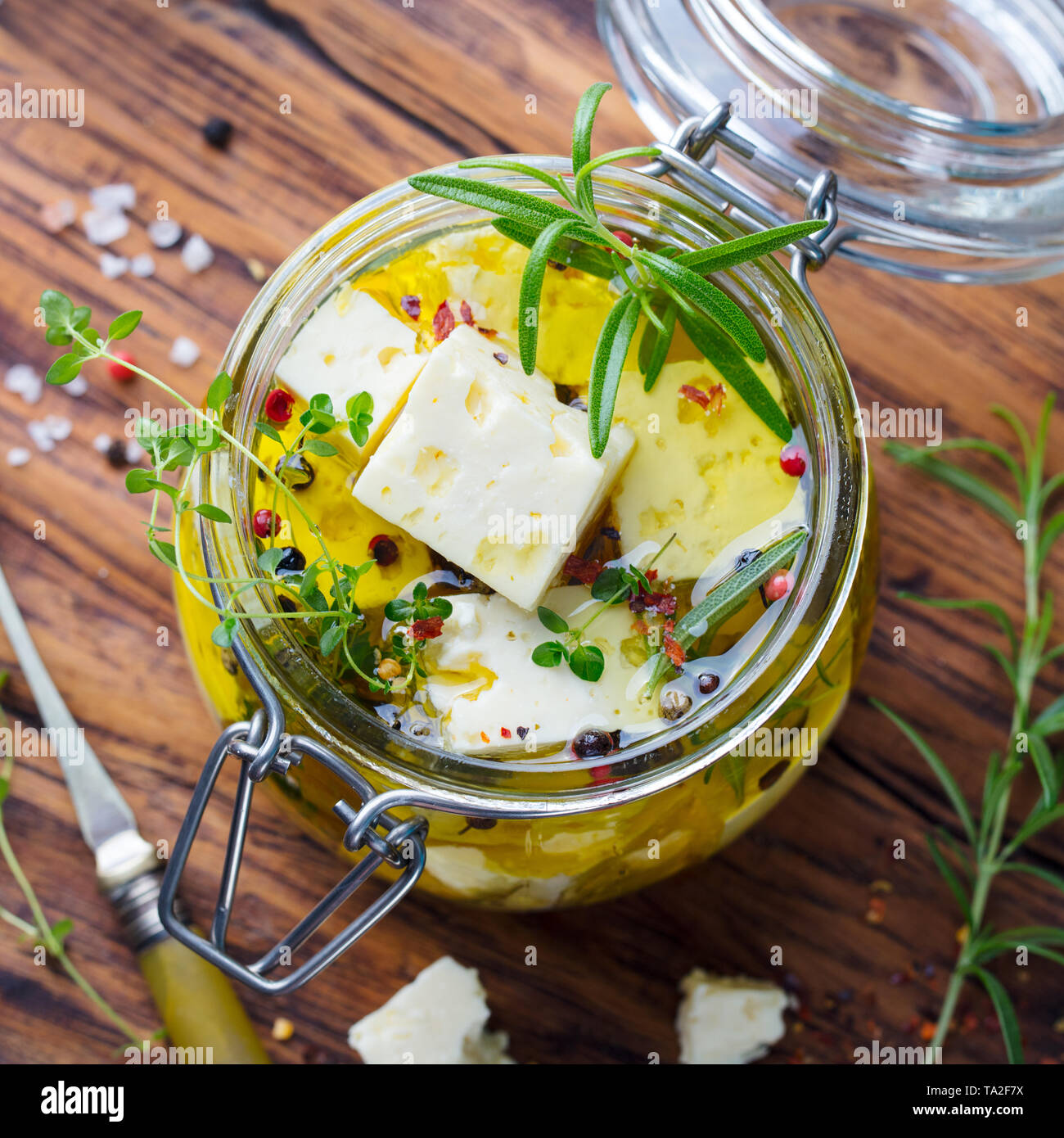 Le fromage Feta mariné à l'huile d'olive avec des herbes fraîches dans un bocal en verre. Fond de bois. Vue d'en haut. Banque D'Images