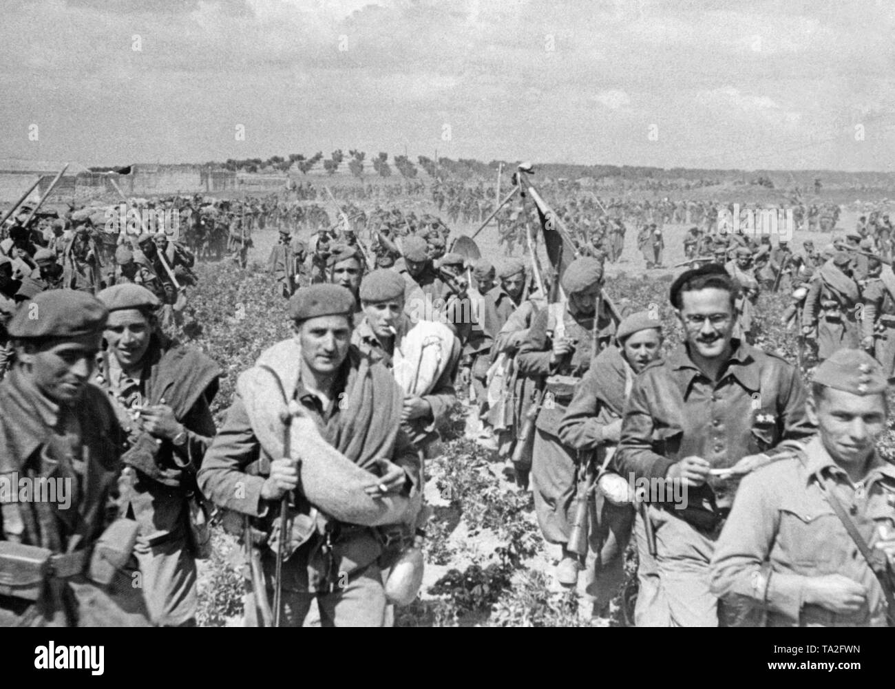 Photo de soldats d'une unité d'alimentation des troupes de Franco marchant à Tolède, Castille la Manche à la fin de mars 1939. Les soldats portent l'équipement en marche et effectuer les drapeaux régimentaires et standard. Ils sont armés de mousquetons. Sur le droit à l'avant, un officier de grade de capitaine (capitaine), derrière lui un lieutenant Teniente () en veste en cuir et beret avec lunettes. Dans l'arrière-plan sont d'oliviers. Banque D'Images