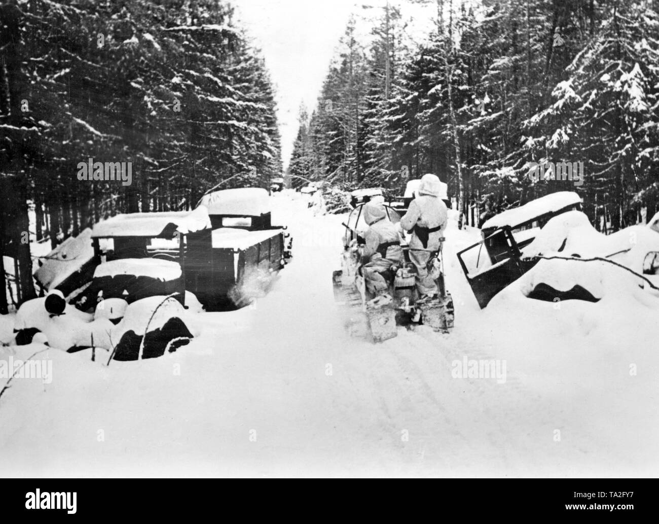 Soldats allemands en collecte de vêtements d'hiver sur une petite Kettenkrad (demi-piste moto) type HK 101 (SD.KFZ. 2) sur une route enneigée sur le front de l'Est. À gauche et à droite, plus de neige-couvertes et probablement détruit des véhicules. Photo de l'entreprise de propagande (PK) : correspondant de guerre Schroeter. Banque D'Images