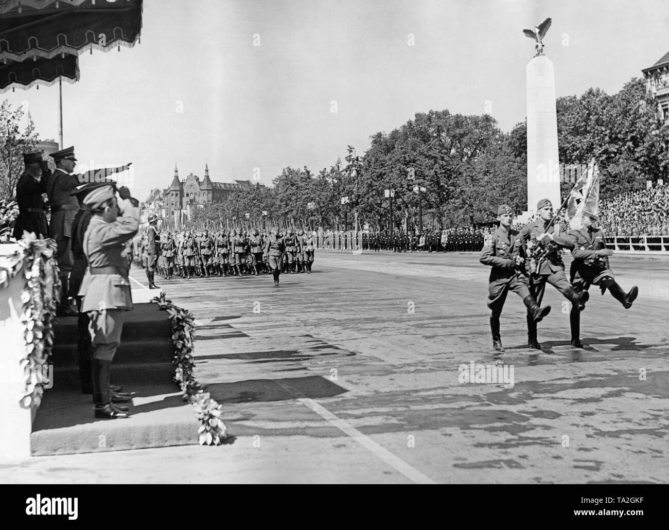 Photo d'un color guard de la légion Condor marchant devant des officiers de la Wehrmacht et Adolf Hitler (sous un auvent, sur la gauche, commandant le général de Wolfram Freiherr von Richthofen) sur l'axe est-ouest (ex-Chalottenburger Chaussee, aujourd'Strasse des 17. Juni ) en face de la Technische Universitaet le 6 juin 1939. Dans l'arrière-plan Le Grandhotel Am Knie (aujourd'hui Ernst Reuter Platz). Banque D'Images