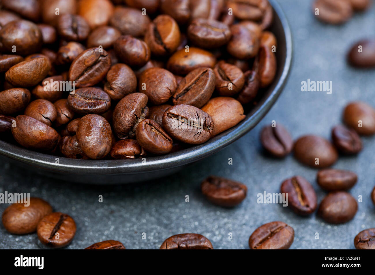 Grains de café dans un bol noir sur fond gris ardoise. Close up. Banque D'Images