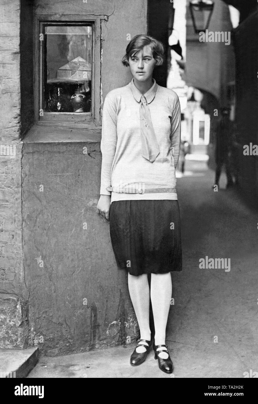 Une jeune femme avec jupe plissée noire et cravate appuyé contre une vieille façade de maison. Banque D'Images