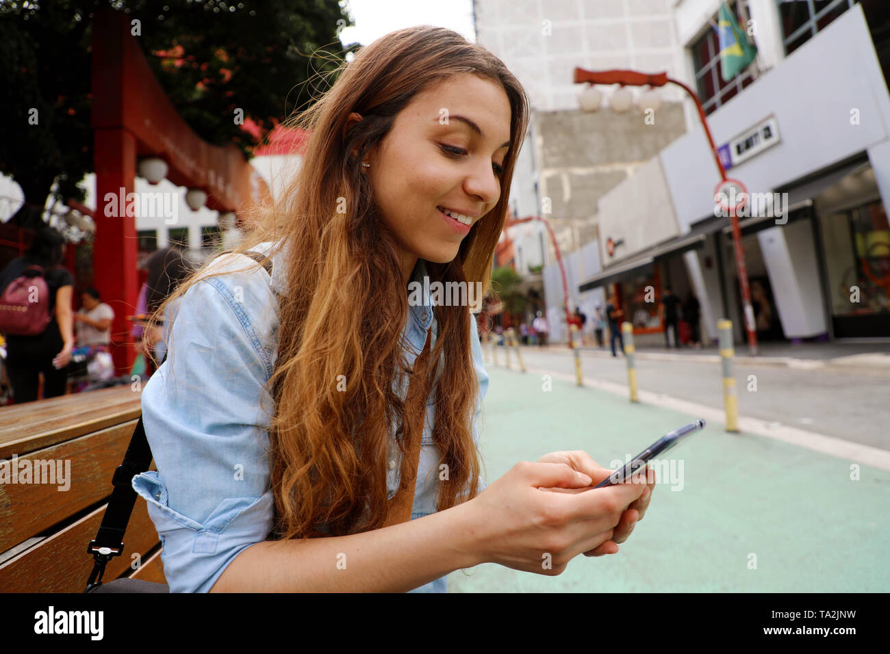 Belle étudiante fille assise sur le banc de la rue avec la messagerie téléphone mobile à Sao Paulo, Brésil Banque D'Images