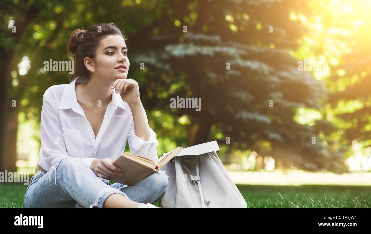 Une photo de femme assise sur l'herbe avec livre et rêver Banque D'Images