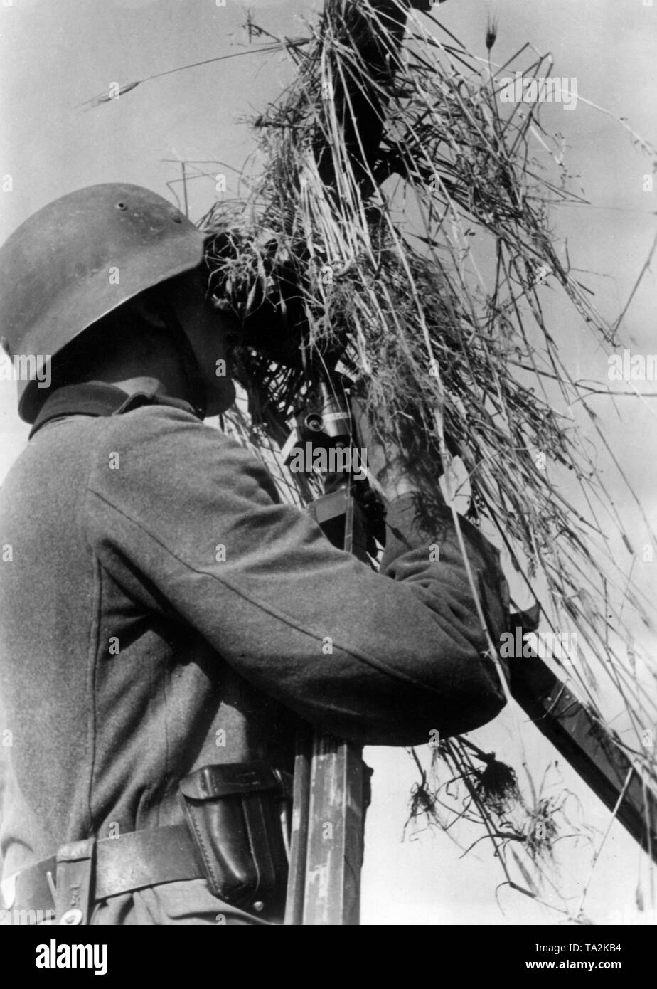 Un membre de la Wehrmacht à un poste de commandement du bataillon observe l'Armée Rouge à l'aide d'un télescope sur le front de l'Est. Banque D'Images