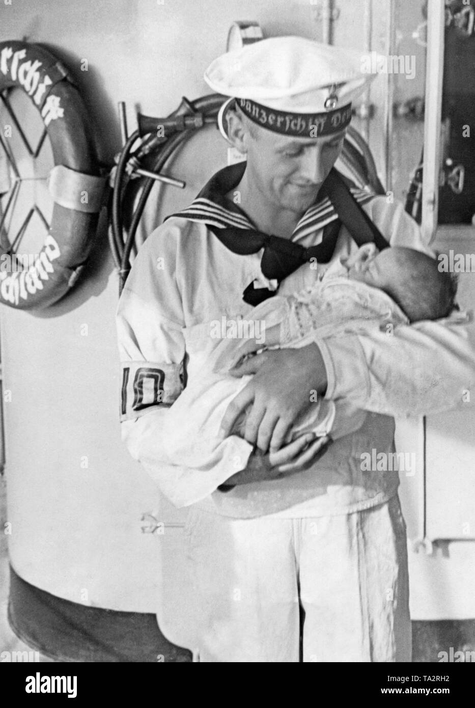 Photo d'un marin tenant un bébé dans ses bras sur le pont du croiseur lourd « Deutschland gisant dans les rues de Valence en Espagne durant la guerre civile en août 1936. La France a apporté à des réfugiés allemands Gérone, où elles ont été prises en charge par le vapeur de l'organisation Nazie Kraft durch Freude ('force par la joie") Monte Sarmiento (lancé en 1924, Monte-Klasse, coulé en 1942). Banque D'Images